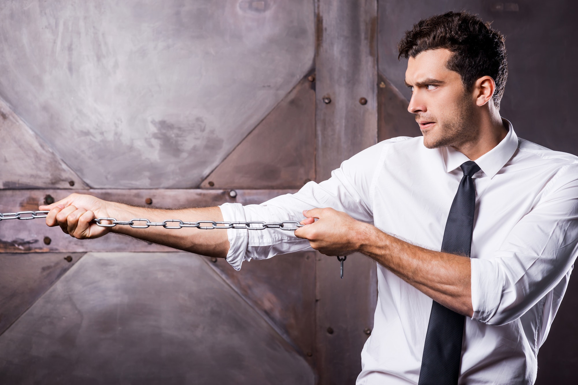 Everyday struggling. Side view of concentrated young man in shirt and tie stretching a chain